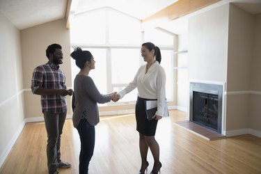Young couple buying new house, handshaking with realtor in agreement