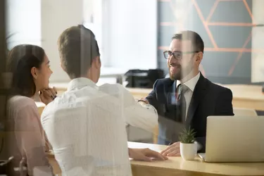 Male realtor handshaking clients after successful negotiations in office