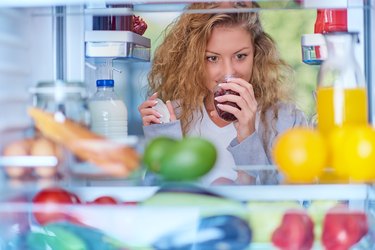 Woman smelling jam in front of fridge full of groceries.