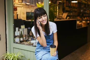 Smiling woman sitting at entrance door of a store talking on cell phone