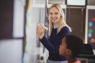 Portrait of teacher assisting schoolboy on whiteboard in classroom