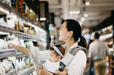 Beautiful Asian woman carrying cute baby girl shopping for organic green marketing products in grocery store
