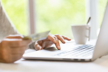 Woman indoors using credit card and laptop. Shopping online.