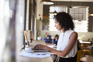 Businesswoman By Window Working On Laptop In Coffee Shop