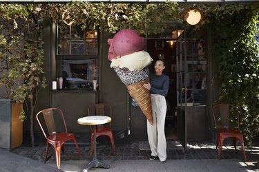 Smiling woman carrying large ice cream cone at sidewalk cafe