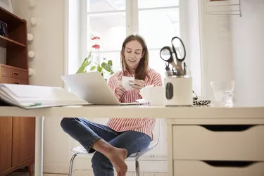 Full length of young woman examining financial bill while working from home