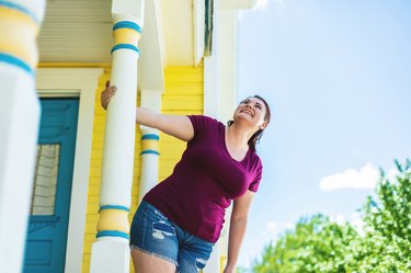 Millennial Female with Reddish Brown Hair Color holding onto Front Porch Decorative Post