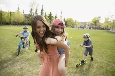 Playful mother piggybacking daughter in sunny park