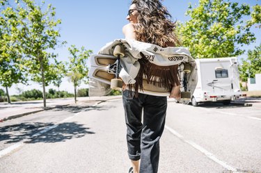 Carefree young woman carrying skateboard in the street, rear view
