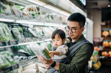 Young Asian father with cute little daughter grocery shopping for fresh organic vegetables in supermarket