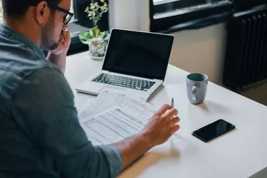 Serious pensive thoughtful focused young casual businessman or entrepreneur in office filling income tax return papers documents for IRS