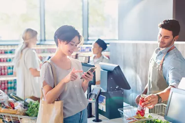 Young woman using cell phone at grocery store market checkout