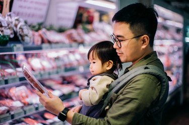Young Asian father with cute little daughter grocery shopping for fresh poultry in supermarket