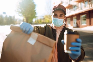Courier in protective mask and medical gloves delivers takeaway food and coffee.