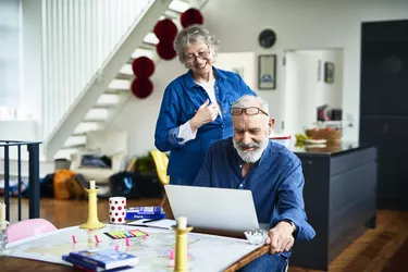 Cheerful retired couple at home planning vacation and man using laptop