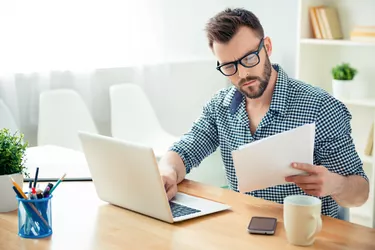 Portrait of concentrated businessman in glasses with laptop reading contract