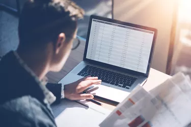 Closeup view of banking finance analyst in eyeglasses working at sunny office on laptop while sitting at wooden table.Businessman analyze stock report on notebook screen.Blurred background,horizontal.