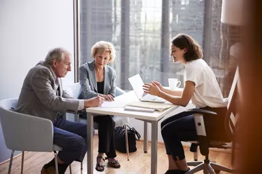 Senior Couple Signing Document In Meeting With Female Financial Advisor In Office