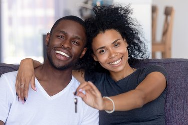 African couple sitting on couch holding keys from new house