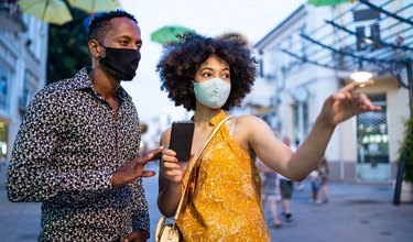 Afro Couple wearing protective face mask walking on the streets and using smart phone, during COVID-19