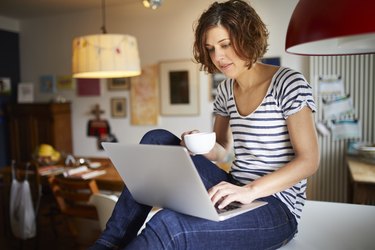 woman sitting on kitchen table using laptop