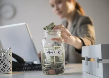 Businesswoman putting money into 401K jar at desk