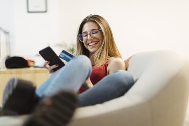 Happy young woman using smartphone and credit card in the office