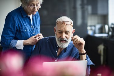 Hipster senior man with beard using laptop and woman watching