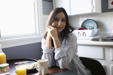 Portrait confident young Latinx woman eating breakfast in kitchen