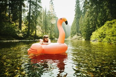 Portrait of laughing woman floating down river on inflatable pink flamingo