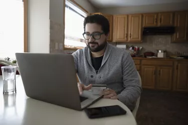 Latinx man with credit card online shopping at laptop in kitchen
