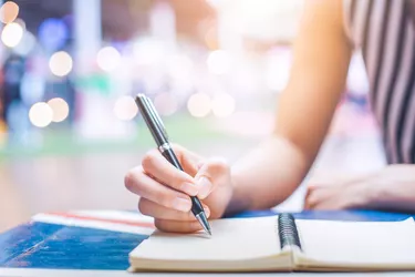 Woman's hand writing on a notebook with a pen on a wooden desk.