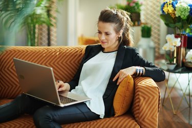 elegant housewife surfing web on laptop while sitting on divan