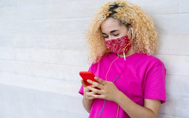 Millenial girl using mobile phone while wearing face mask during coronavirus outbreak - Female teenager having fun with new trends technology - Covid 19 lifestyle - Focus on eyes