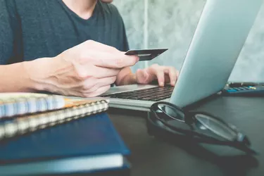 Casual young man holding credit card and using laptop on the desk