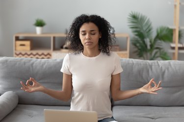 Focused black woman meditating on sofa at home