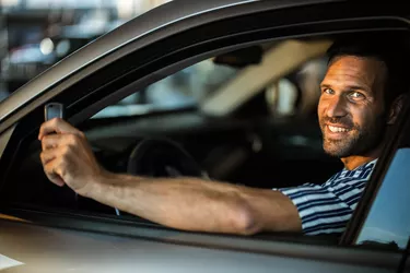 Young happy man with his keys inside of a car.