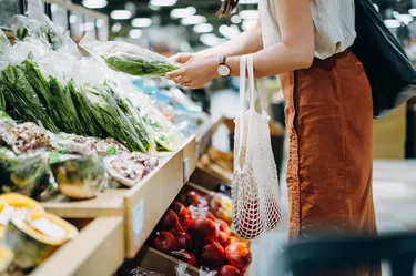 Cropped shot of young Asian woman shopping for fresh organic groceries in supermarket. She is shopping with a cotton mesh eco bag and carries a variety of fruits and vegetables. Zero waste concept