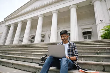 University student sitting outside on steps and using laptop