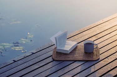cup of coffee and book on wooden pier on summer lake
