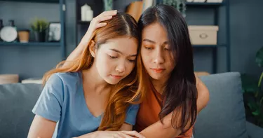Asian women teenager embracing to calm her sad best friends from feeling down from breakup with boyfriend in living room at home. Friendship counseling and care, unhappy girl support her girlfriend.