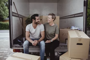 Smiling male and female partners looking at each other while sitting by cardboard boxes in van