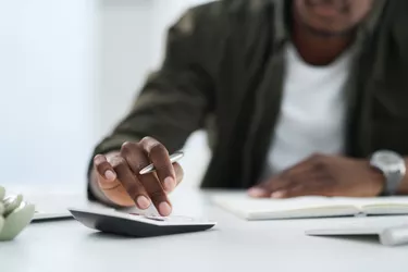 Cropped shot of a young man using a calculator at work