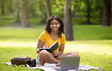 Smiling black girl studying online on laptop at summer park