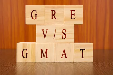 Concept of GRE vs GMAT Exam differences in wooden block letters on table.