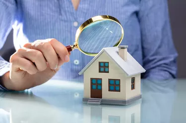 Businesswoman Holding Magnifying Glass Over House Model