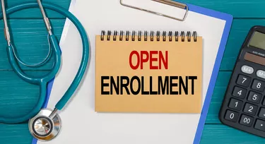 Notepad with text OPEN ENROLLMENT, calculator and stethoscope.