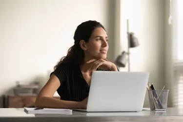 Smiling thoughtful female employee working at laptop from home