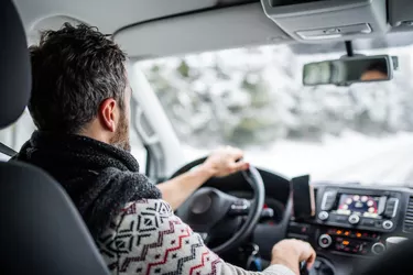 Rear view of mature man driving car on snowy road.