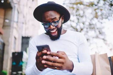 Emotional surprised african american guy with low prices in web store receiving message with promo code,excited dark skinned hipster guy in trendy hat overjoyed with winning online contest on web site